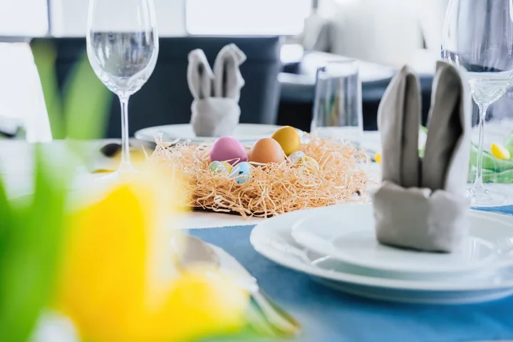 Stół wielkanocny z gniazdem ze słomy i kolorowymi pisankami, serwetki złożone jak uszy zająca