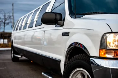 Biała, długa limuzyna typu SUV widziana z boku, z zapalonym przednim reflektorem.