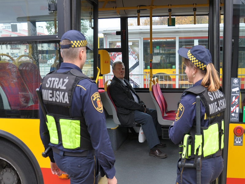 Zdjęcie ilustracyjne- strażnicy miejscy przy wejściu do autobusu. Wewnątrz siedzi starszy mężczyzna
