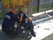 Strażnik miejski opatruje zranioną głowę mężczyzny siedzącego w wiacie przystankowej.