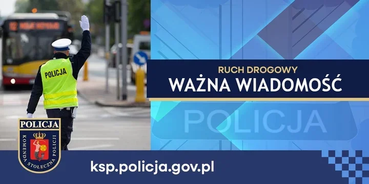Policjant w kamizelce odblaskowej z napisem POLICJA kieruje ruchem drogowym na ulicy, w tle autobus miejski.