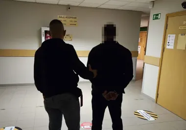 Dwóch mężczyzn w korytarzu przed salami rozpraw, jeden z nich ma założone kajdanki.