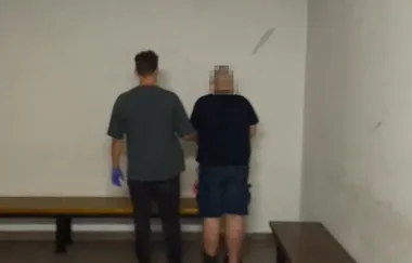 Funkcjonariusz w niebieskiej rękawiczce prowadzi zatrzymaną osobę w pomieszczeniu z ławkami.