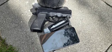 Na chodniku leży pistolet, magazynek z nabojem gazowym oraz smartfon obok słupa.