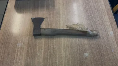 Siekierka z drewnianym trzonkiem owiniętym folią leży na brązowym blacie.