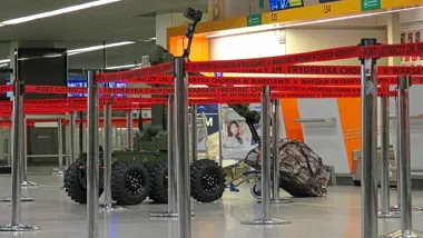 Wewnątrz warszawskiego lotniska Chopina stoi wojskowy robot rozpoznawczy za czerwoną taśmą odgradzającą stanowiska odpraw.