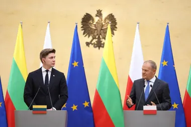 Dwaj mężczyźni w garniturach stoją przy mównicach z flagami Litwy, Polski i Unii Europejskiej w tle podczas konferencji prasowej.