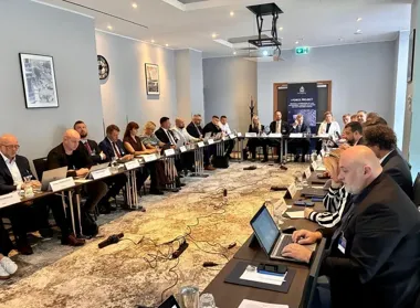 Uczestnicy konferencji lub spotkania roboczego projektu I-FORCE organizowanego przez Interpol siedzą przy stołach w sali konferencyjnej z laptopami i dokumentam