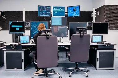 Operator siedzi przy stanowisku z wieloma monitorami w nowoczesnym centrum kontroli lub nadzoru.