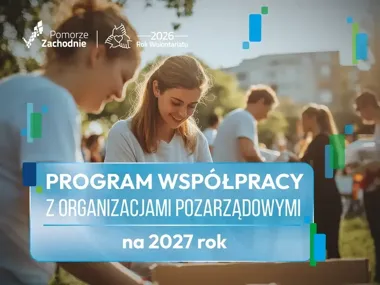 Młodzi wolontariusze w białych koszulkach sortują produkty z kartonów podczas plenerowej akcji charytatywnej na trawniku w słoneczny dzień.
