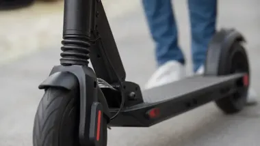 Zbliżenie na przednią część czarnej hulajnogi elektrycznej stojącej na chodniku.