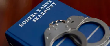 Kajdanki leżą na niebieskim egzemplarzu Kodeksu karnego skarbowego.