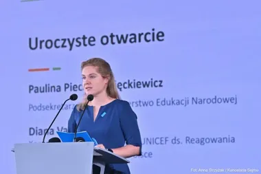 Kobieta w niebieskiej sukience przemawia z mównicy podczas uroczystego otwarcia wydarzenia.