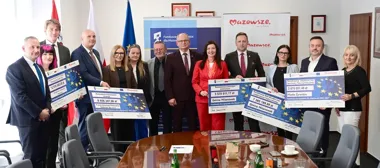 Grupa osób w siedzibie samorządu województwa mazowieckiego odbiera symboliczne czeki z funduszy europejskich na projekty lokalne.
