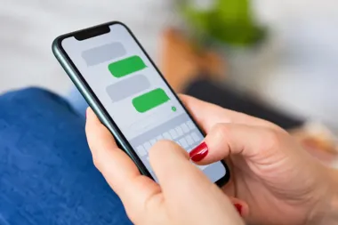 Kobieta z czerwonym manicure trzyma smartfona i pisze wiadomość tekstową na ekranie z klawiaturą dotykową.