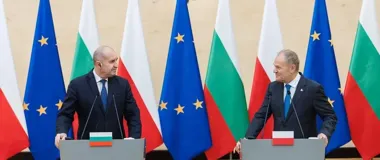 Dwaj mężczyźni w garniturach stoją przy mównicach z flagami Polski, Bułgarii i UE w tle podczas konferencji prasowej.