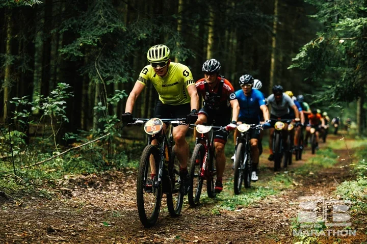Grupa rowerzystów górskich jedzie ścieżką przez las podczas maratonu MTB.